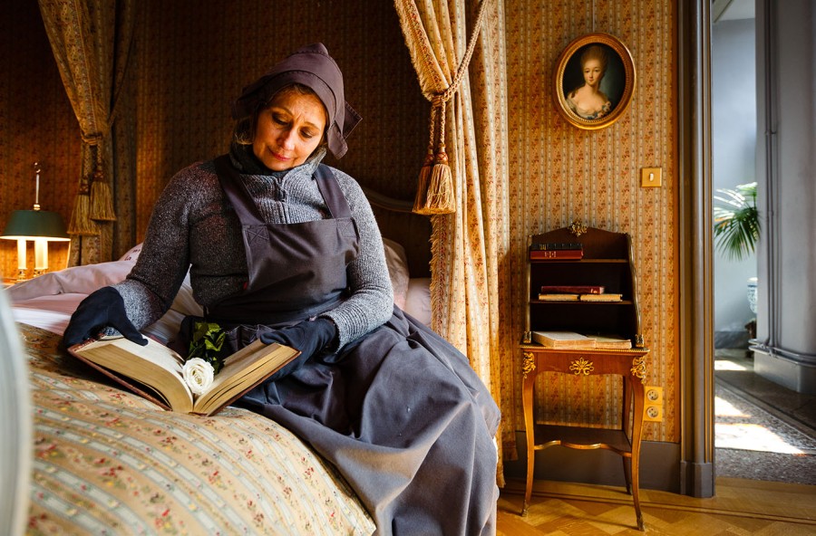 Foto van een vrouw die leest in een groot boek op het bed in de slaapkamer van de markiezin